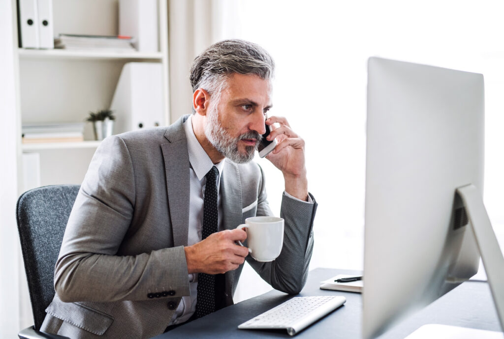 businessman with smartphone, coffee and computer sitting at the table, making a phone call.